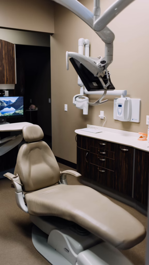 Dental operatory chair and overhead dental equipment in a treatment room with a computer monitor in the background, ready for a patient.