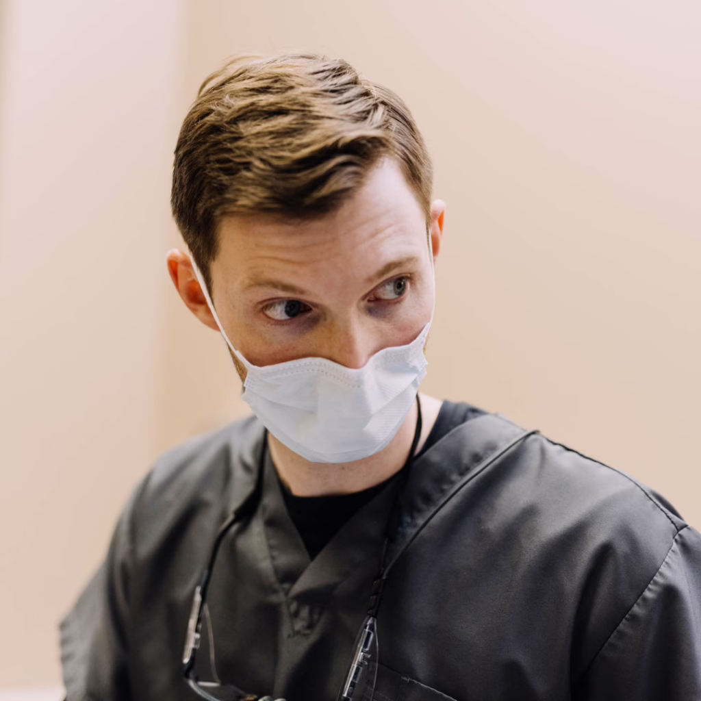 Healthcare professional in gray scrubs wearing a surgical mask, looking to the right.